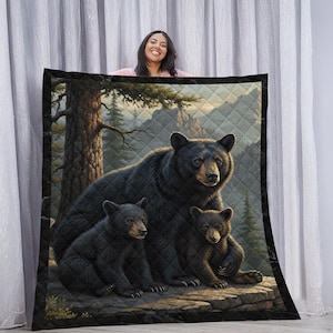 May include: A quilted blanket featuring a detailed illustration of a black bear family in a forest setting. The image shows a mother bear with two cubs, set against a backdrop of trees and mountains. The blanket has a black border.