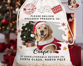 May include: A white drawstring Christmas gift bag featuring a Golden Retriever wearing a Santa hat and suit. The bag includes the text "Please deliver enclosed presents to: Cooper" and "Santa Mail" stamps.