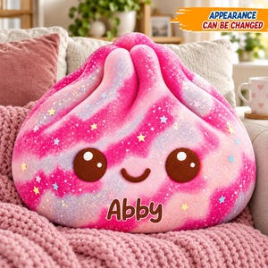 May include: A plush dumpling-shaped pillow featuring a pink and white tie-dye pattern with glittery star accents. The pillow has two large brown eyes, a small smile, and the name Abby printed in brown text. The text Appearance Can Be Changed is visible.