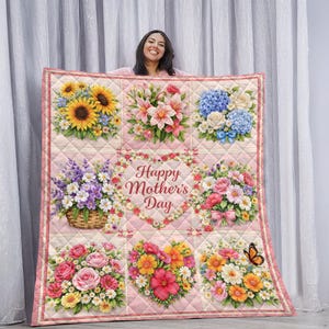 May include: A quilted blanket featuring a floral design with sunflowers, lilies, hydrangeas, and roses. The blanket has a pink border and a central heart-shaped floral arrangement with the text "Happy Mother's Day". A butterfly is also visible.