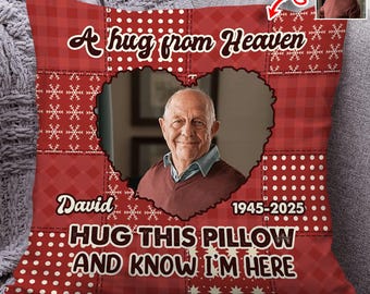 Puede incluir: Cojín decorativo rojo con una foto de un hombre mayor en un marco en forma de corazón. El cojín tiene el texto "A hug from Heaven", el nombre "David" y los años "1945-2025". El texto "HUG THIS PILLOW AND KNOW I'M HERE" también está presente.