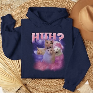 K&ouml;nnte beinhalten: Marineblauer Hoodie mit einem wei&szlig;en Katzen-Meme-Bild und dem Text "HUH?" auf der Vorderseite.