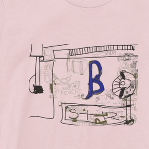 May include: A pink t-shirt with a black and white graphic design of a stylized drawing of a stereo system with the letter "B" in blue. The design includes the words "SUB", "KEOCAT", "WGAM", and "STR".