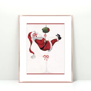 Op de afbeelding: Een vintage kerst-illustratie van Sinterklaas die ondersteboven hangt in een martini-glas met een olijf. De illustratie is in een wit frame met een gouden rand.