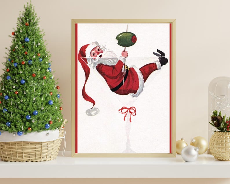 Op de afbeelding: Een vintage kerst-illustratie van Sinterklaas die ondersteboven hangt in een martini-glas met een olijf. De illustratie is in een gouden lijst.