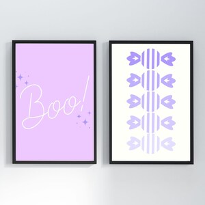 May include: Two framed prints with a Halloween theme. The first print has a light purple background with the word "Boo!" in white cursive. The second print has a white background with a pattern of purple candy canes.