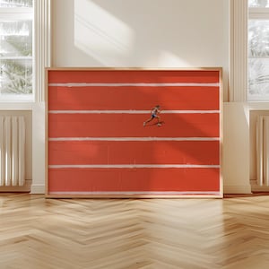 May include: Framed artwork featuring a runner on a red track with white lanes. The runner is wearing blue and white athletic attire. The artwork is displayed in a room with hardwood floors and windows.