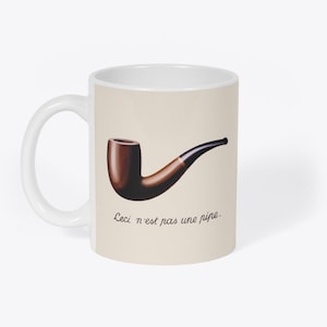 May include: White ceramic mug featuring an illustration of a brown pipe and the text "Ceci n'est pas une pipe."