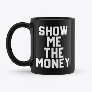 以下が含まれることがあります： 白い文字で「SHOW ME THE MONEY」と書かれた黒いセラミック製のコーヒーカップです。