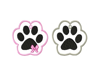 May include: Two paw print shaped tags, one with a pink outline and a pink bow, the other with a gray outline. Both have a black paw print in the center.