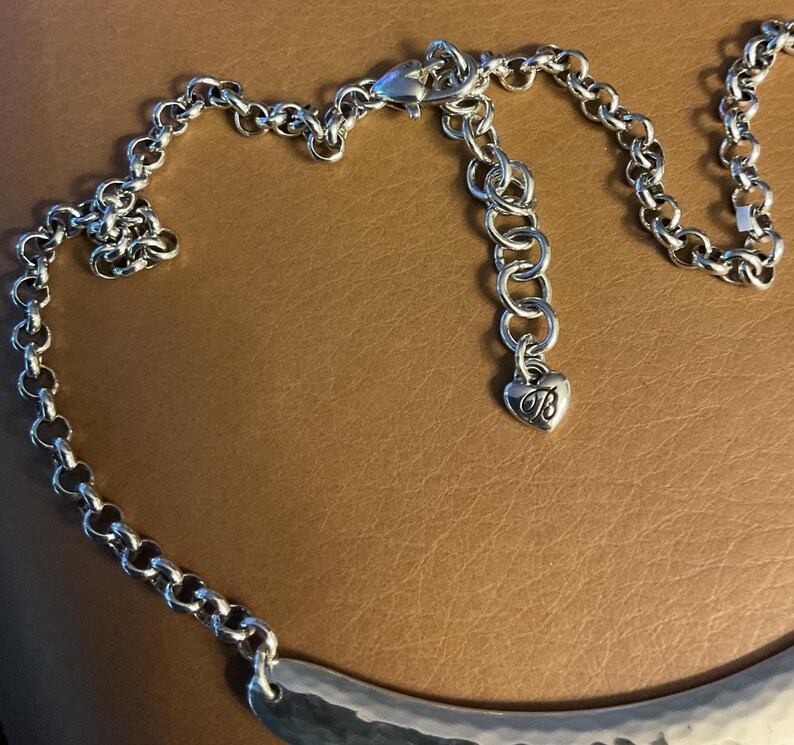 Puede incluir: Collar plateado con un colgante de metal martillado. El collar presenta una cadena con un cierre de mosquet&oacute;n y una extensi&oacute;n ajustable. Un peque&ntilde;o dije en forma de coraz&oacute;n con la letra "B" cuelga de la extensi&oacute;n.