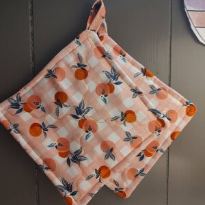 May include: Two pink and white quilted pot holders with a peach and leaf pattern. The pot holders have a loop for hanging.