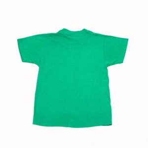 K&ouml;nnte beinhalten: Ein einfarbiges gr&uuml;nes T-Shirt mit kurzen &Auml;rmeln. Das T-Shirt hat einen Rundhalsausschnitt und besteht aus einem weichen, strukturierten Stoff. Das T-Shirt ist in einem leuchtenden Gr&uuml;nton gehalten, wahrscheinlich aus Baumwolle oder einem &auml;hnlichen Material.