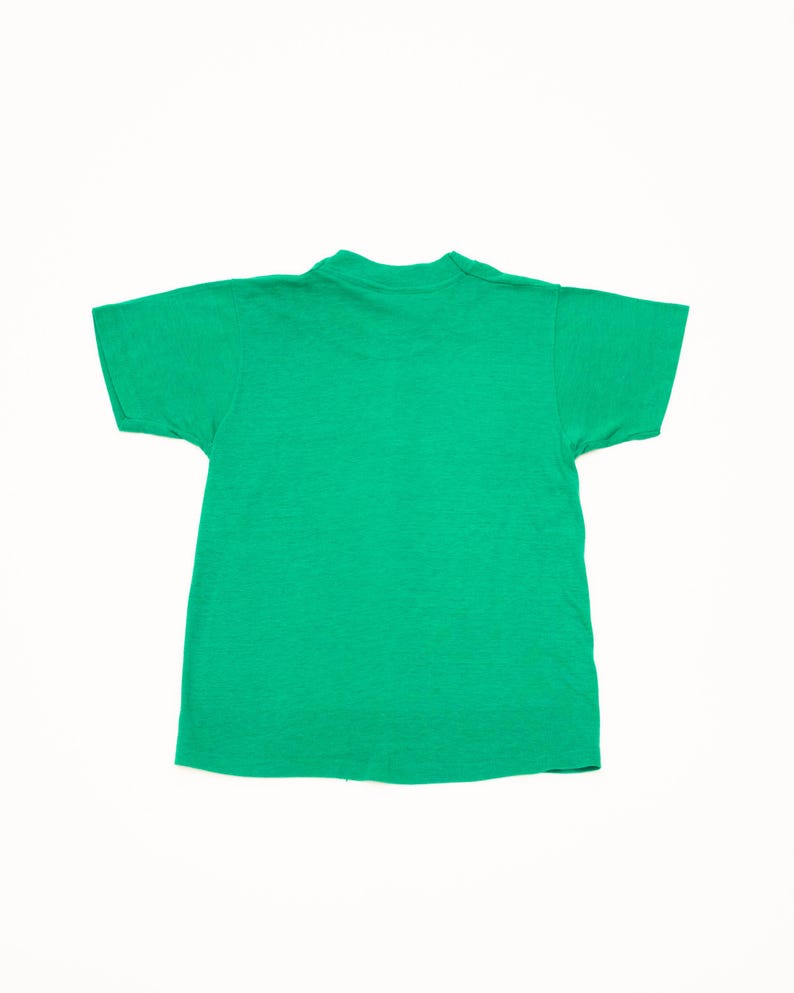 K&ouml;nnte beinhalten: Ein einfarbiges gr&uuml;nes T-Shirt mit kurzen &Auml;rmeln. Das T-Shirt hat einen Rundhalsausschnitt und besteht aus einem weichen, strukturierten Stoff. Das T-Shirt ist in einem leuchtenden Gr&uuml;nton gehalten, wahrscheinlich aus Baumwolle oder einem &auml;hnlichen Material.