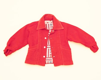 May include: A vibrant red corduroy jacket with a wide collar and button fastening. The jacket features two front pockets and long sleeves with buttoned cuffs. The interior lining displays a geometric pattern in red, white, and blue.