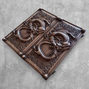 Könnte beinhalten: Bronzefarbene, verzierte Türpaneele mit detaillierten Drachenreliefs. Die rechteckigen Paneele weisen aufwendige florale und geometrische Muster um die Drachen herum auf. Die Drachen sind in einer gewundenen Pose dargestellt, was dem Design Dynamik verleiht.