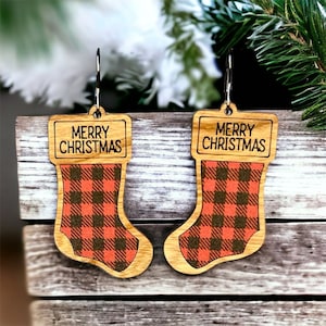 Könnte beinhalten: Ein Paar Ohrringe aus Holz in Form von Weihnachtsstrümpfen mit einem rot-schwarzen Karomuster und dem Schriftzug "Frohe Weihnachten" auf jedem Strumpf.