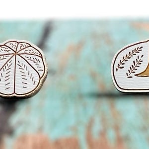 Puede incluir: Cuatro pendientes de madera con diferentes diseños. Dos pendientes presentan un diseño geométrico blanco y marrón, y los otros dos pendientes presentan un diseño blanco y marrón de una hoja con un centro marrón.