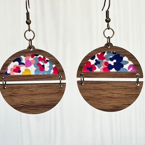 May include: A pair of wooden earrings with a floral pattern. The earrings are made of two pieces of wood, one with a floral pattern and the other plain. The floral pattern is in shades of pink, blue, and yellow.