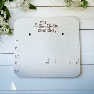 May include: White wooden growth chart with a ruler marked in half-inch increments up to 2.5 inches. The chart has two holes at the top and the text "THE thankful CREATIONS" in brown lettering.