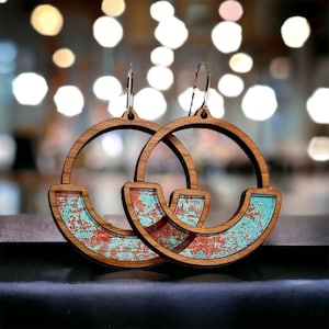 Puede incluir: Pendientes de aro de madera con incrustaciones estampadas en turquesa y rojo. Los pendientes tienen un diseño circular con una incrustación en forma de media luna. Cuelgan de ganchos plateados.