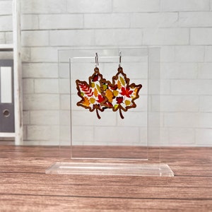 May include: A pair of maple leaf earrings with a fall leaf pattern. The earrings are made of wood and have silver hooks.