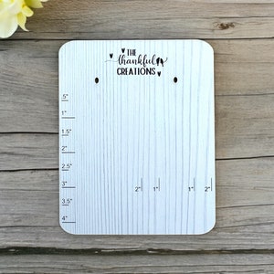May include: White wooden board with a ruler marked in inches, two holes, and the text "THE thankful CREATIONS" with hearts and birds.