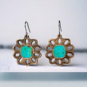 May include: A pair of wooden earrings with a turquoise blue center and a delicate, floral design.