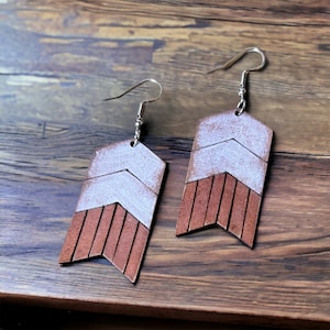 May include: A pair of brown leather earrings with a white chevron pattern. The earrings have silver hooks.
