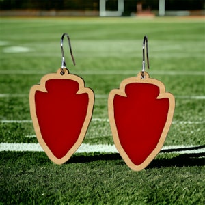 May include: A pair of red and brown arrowhead-shaped earrings. The earrings are made of wood and have a red paint finish.