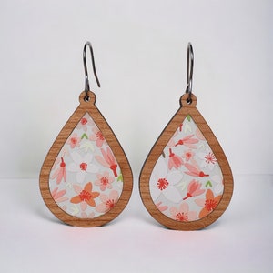 May include: A pair of teardrop-shaped wooden earrings with a floral pattern. The earrings are light gray with pink and orange flowers. The earrings have silver hooks.