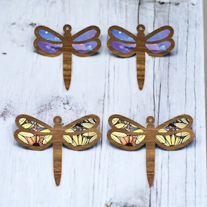 May include: Four wooden dragonfly ornaments with different designs. Two have a purple and blue galaxy design and two have a yellow and orange floral design.