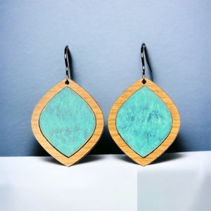 May include: A pair of turquoise blue and natural wood earrings. The earrings are shaped like a teardrop and have a silver hook.