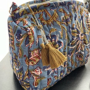 May include: A quilted cosmetic bag in a light blue fabric with a floral pattern in red, green, and navy. The bag has a gold zipper and a tassel with gold beads and two gold tassels.