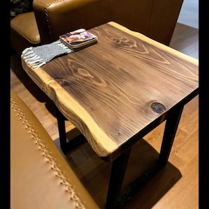 May include: A dark brown wooden end table with a live edge top and black metal legs. The table has a grey woven coaster on top.