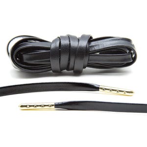 May include: Black leather shoelaces with gold metal tips. The laces are coiled and laid out flat.