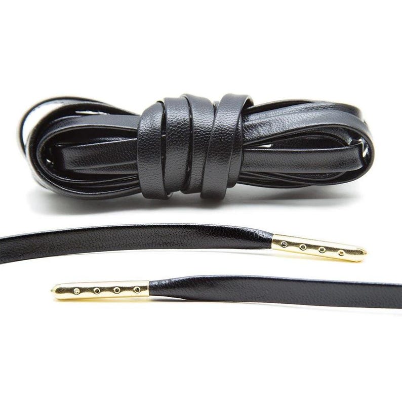 May include: Black leather shoelaces with gold metal tips. The laces are coiled and laid out flat.