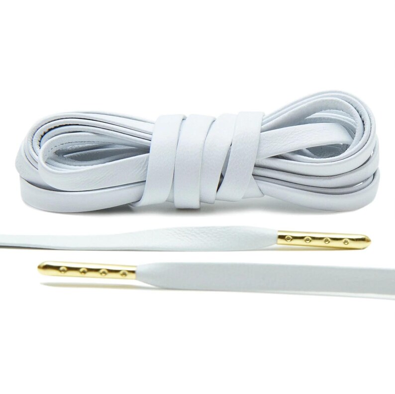 May include: White leather shoelaces with gold aglets. The laces are coiled and laid out flat.