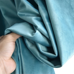 May include: Close-up of a soft, teal blue velvet fabric. The fabric is draped and folded, showing its texture and drape.