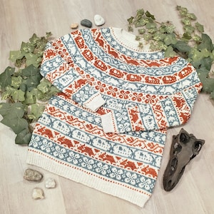 Può includere: Un maglione bianco lavorato a maglia con un motivo geometrico blu e arancione. Il maglione ha una vestibilità ampia e un collo rotondo.