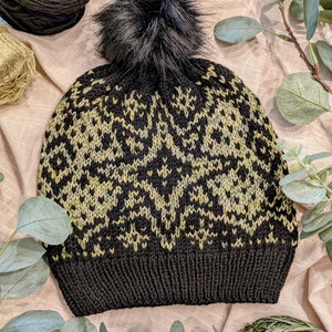 Puede incluir: Gorro de punto negro con un patrón geométrico verde y negro y un pompón de piel sintética negro.