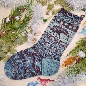 Peut inclure: Une chaussette de Noël tricotée à la main, dans des tons de bleu et de violet foncé, avec des motifs géométriques complexes et un poignet décoratif avec un lien bleu. La chaussette mesure environ 50 cm de long.