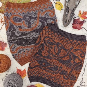 May include: Two knitted cowls with intricate geometric and swirling patterns in shades of gray, brown, and orange. The cowls are displayed on a white surface with fall leaves and yarn balls.