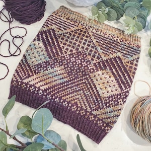 May include: A brown and beige knitted scarf with a geometric pattern. The scarf is made of soft yarn and has a fringed edge.