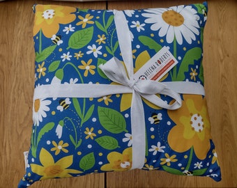 May include: A blue pillow with a floral pattern featuring yellow and white flowers, green leaves, and bees. The pillow is wrapped in white ribbon and has a small tag with the text "HELENA ROBERTS" and a website address.