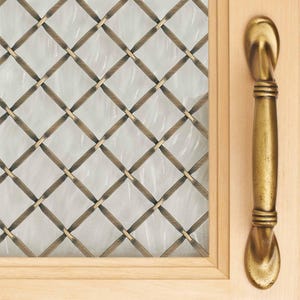 May include: A close-up of a wooden door with a decorative glass panel and a brass handle. The glass panel has a diamond pattern created by intersecting bronze-colored metal strips. The handle is a curved, elongated brass pull.