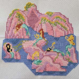 Puede incluir: Bordado de punto de cruz de un paisaje rosa y azul con múltiples figuras en varias poses. Las figuras están hechas de hilo amarillo, verde y rosa.
