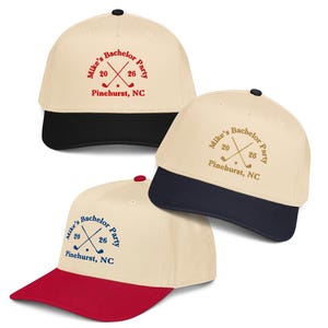 May include: Three baseball caps with a cream-colored crown and a colored brim. Each cap has the text "Mike's Bachelor Party 2026 Pinehurst, NC" with crossed golf clubs. The brims are black, navy, and red.