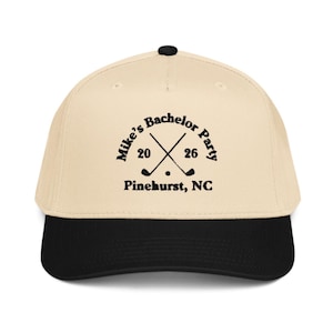 May include: A beige and black baseball cap with the text "Mike's Bachelor Party 2026 Pinehurst, NC" in black. The design includes crossed golf clubs and a golf ball.