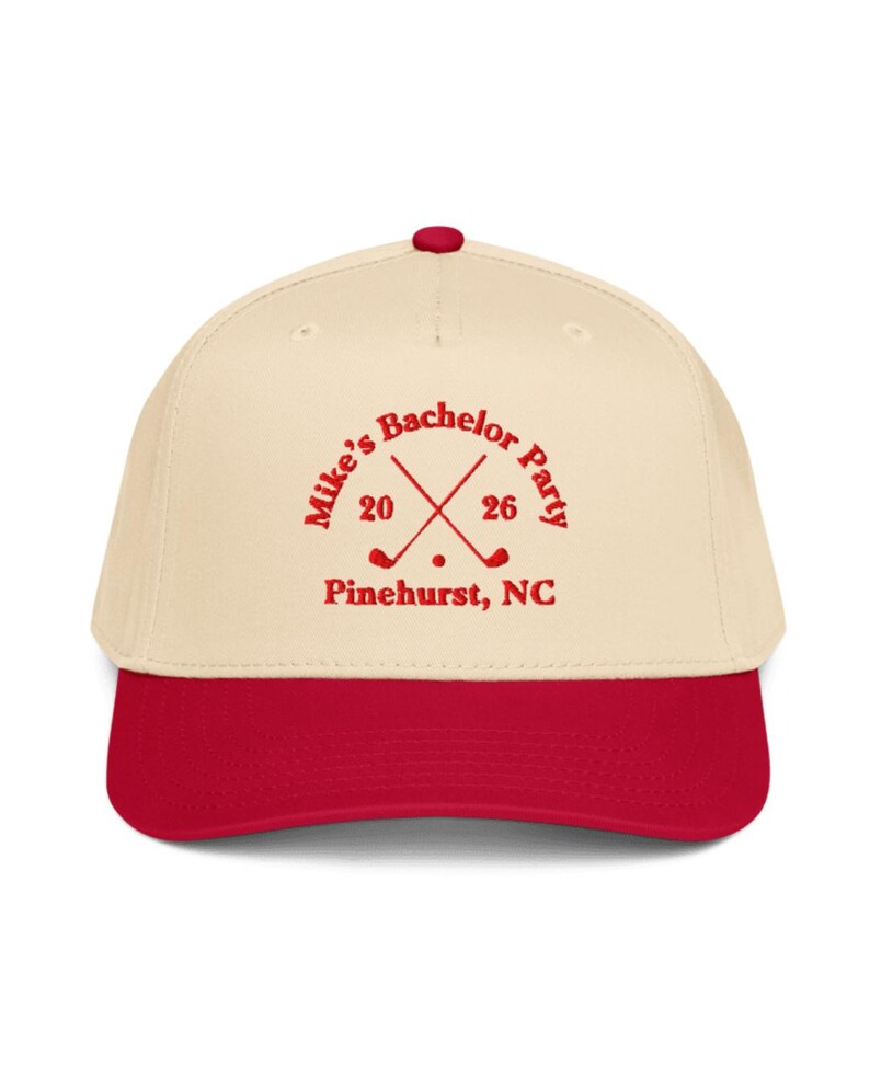 May include: A cream-colored baseball cap with a red brim and button. The cap features the text "Mike's Bachelor Party" in red, along with crossed golf clubs and the numbers "20" and "26". Below the text is "Pinehurst, NC".